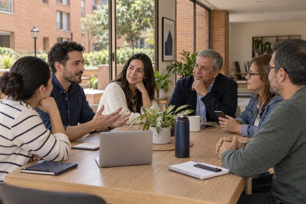 Vecinos participan en una reunión alrededor de una mesa con un computador y un teléfono.